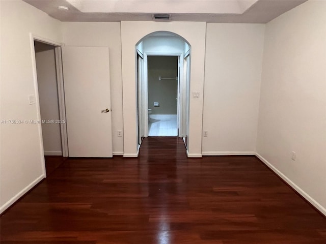 hallway with arched walkways, visible vents, baseboards, and wood finished floors