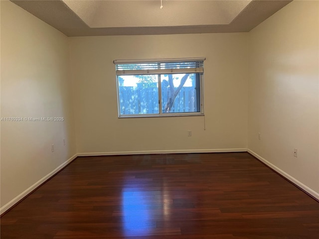 spare room featuring dark wood finished floors, a tray ceiling, and baseboards