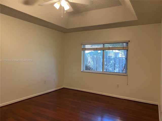 unfurnished room featuring a tray ceiling, a textured ceiling, dark wood finished floors, baseboards, and ceiling fan