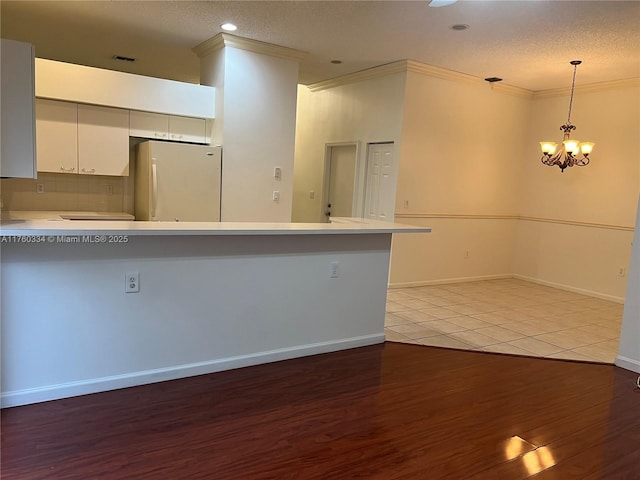 kitchen with light wood finished floors, a peninsula, freestanding refrigerator, light countertops, and crown molding