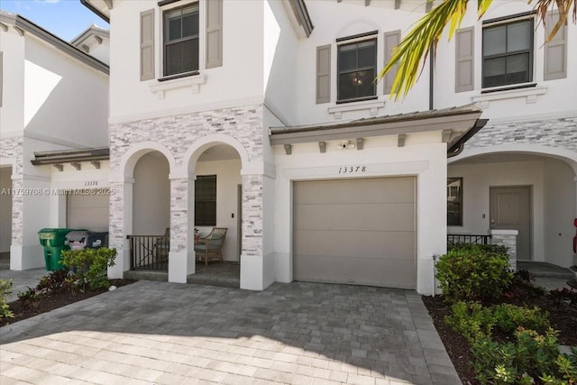 view of front of home with decorative driveway, stone siding, an attached garage, and stucco siding