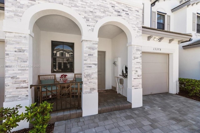 doorway to property with a garage, stone siding, covered porch, and stucco siding