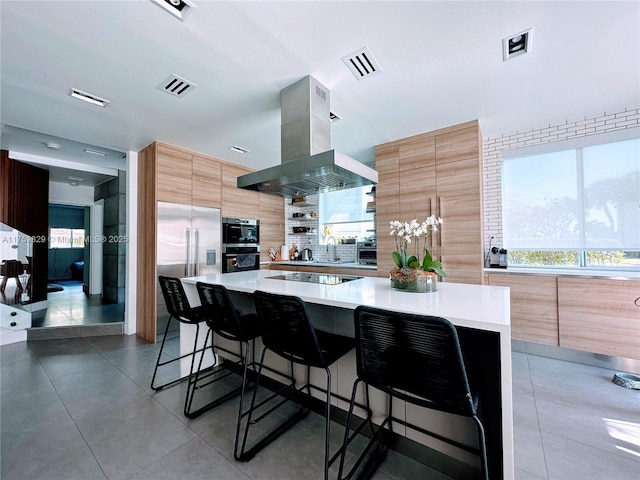 kitchen featuring visible vents, island exhaust hood, appliances with stainless steel finishes, a kitchen bar, and modern cabinets