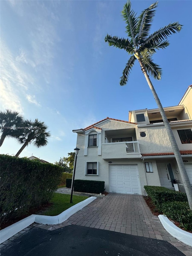 view of property with decorative driveway, a balcony, an attached garage, and stucco siding