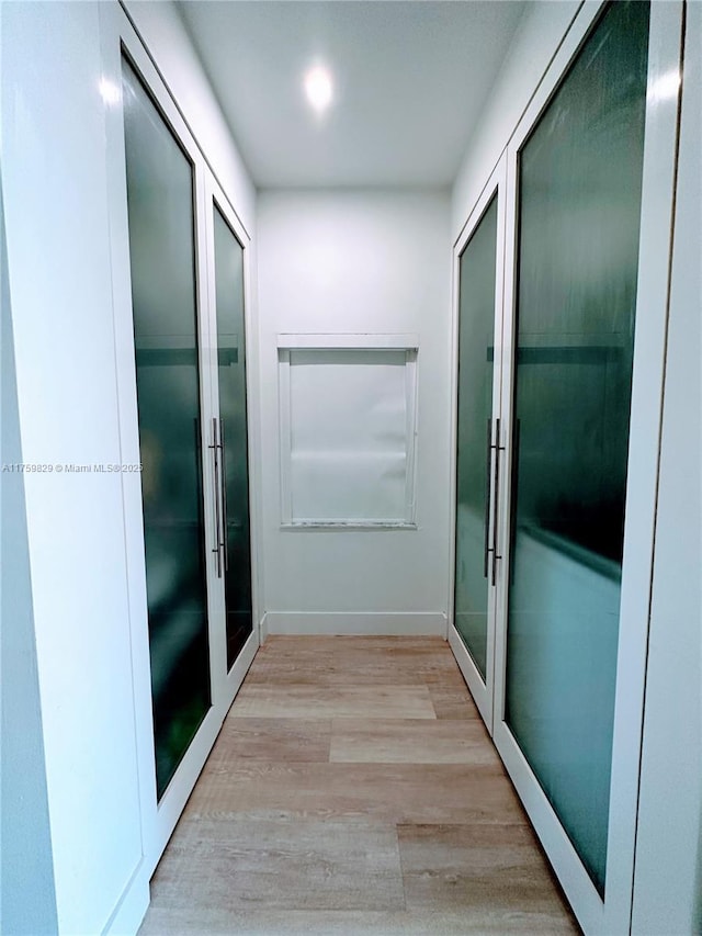 hall with french doors, baseboards, and light wood-style floors