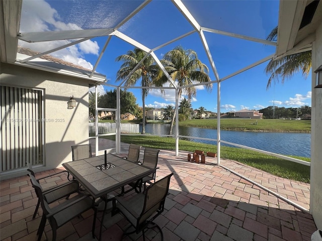 view of patio featuring glass enclosure, a water view, and outdoor dining space