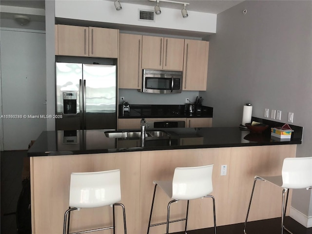 kitchen with visible vents, a sink, dark countertops, stainless steel appliances, and a peninsula