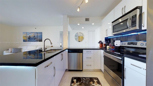 kitchen featuring dark countertops, visible vents, appliances with stainless steel finishes, a peninsula, and a sink