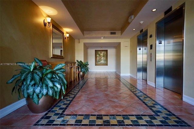 hallway featuring visible vents, baseboards, elevator, a raised ceiling, and tile patterned floors