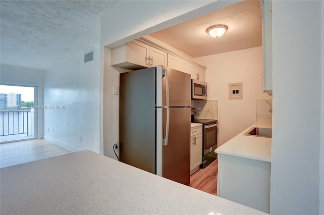 kitchen with stainless steel microwave, freestanding refrigerator, electric stove, white cabinets, and a sink