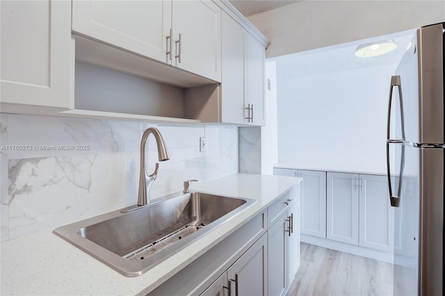 kitchen with light stone countertops, light wood finished floors, a sink, decorative backsplash, and white cabinets