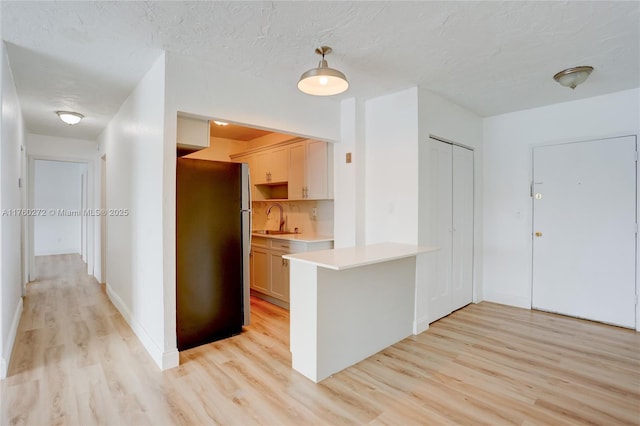 kitchen featuring a peninsula, light wood-style flooring, freestanding refrigerator, a sink, and light countertops