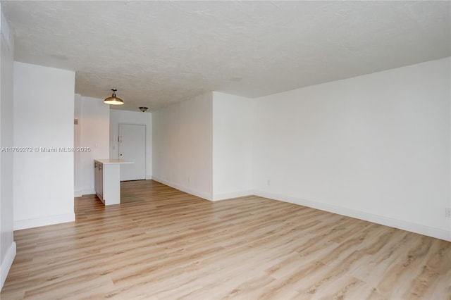 spare room featuring light wood-style flooring, a textured ceiling, and baseboards