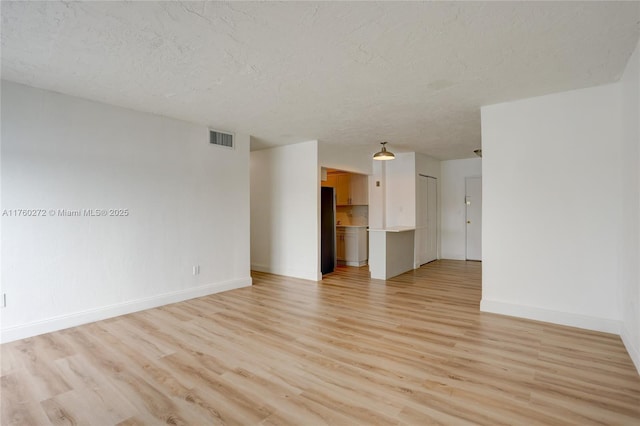 empty room featuring visible vents, baseboards, light wood-style floors, and a textured ceiling