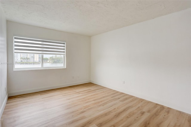 unfurnished room featuring light wood-style floors, baseboards, and a textured ceiling