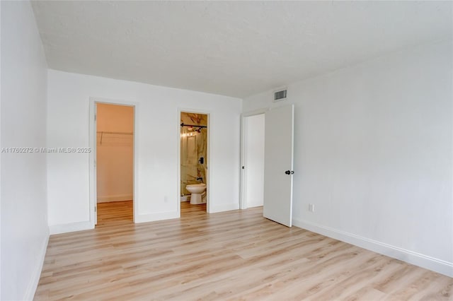 unfurnished bedroom featuring visible vents, a walk in closet, baseboards, light wood-style flooring, and a closet