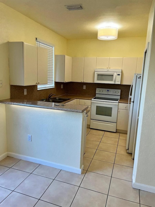 kitchen with white appliances, a peninsula, visible vents, and backsplash