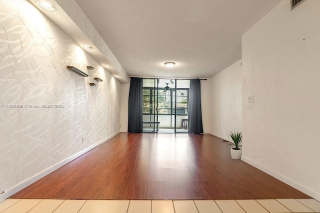 empty room featuring visible vents, a wall of windows, baseboards, and wood finished floors