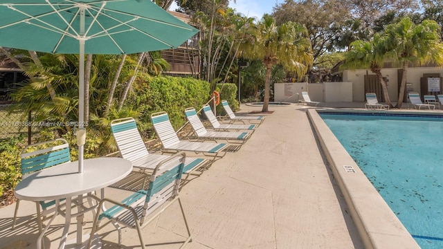 community pool with a patio, a hot tub, and fence