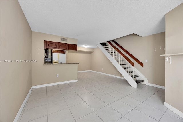 unfurnished living room featuring visible vents, baseboards, a textured ceiling, and stairway