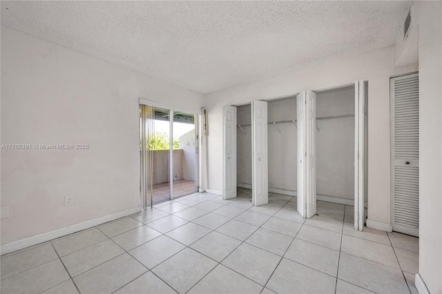 unfurnished bedroom featuring light tile patterned floors, a textured ceiling, two closets, and baseboards