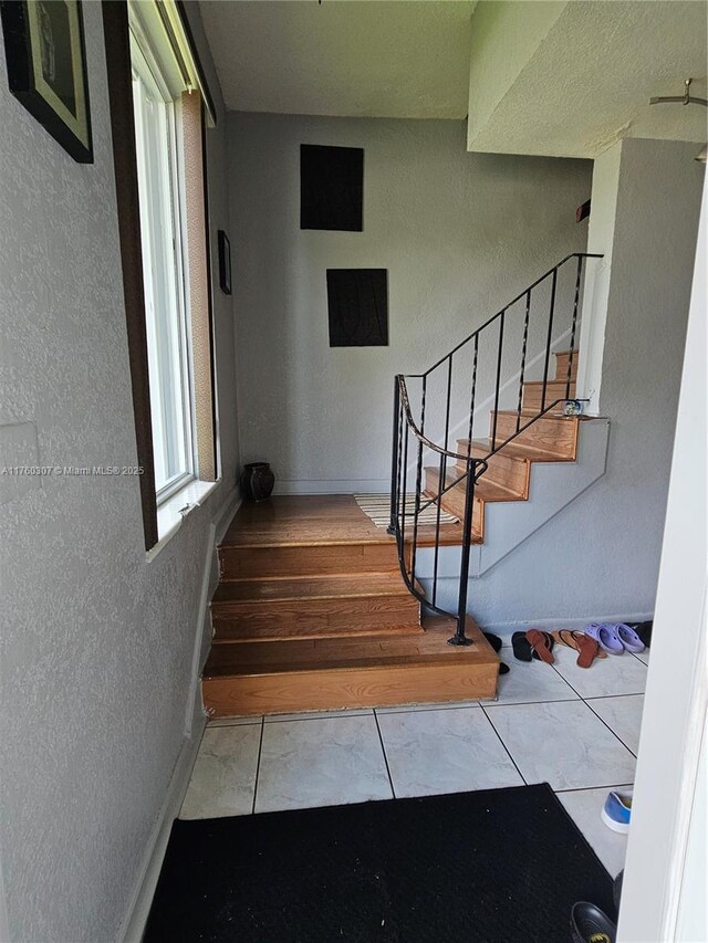 stairway with tile patterned floors, a textured wall, and baseboards