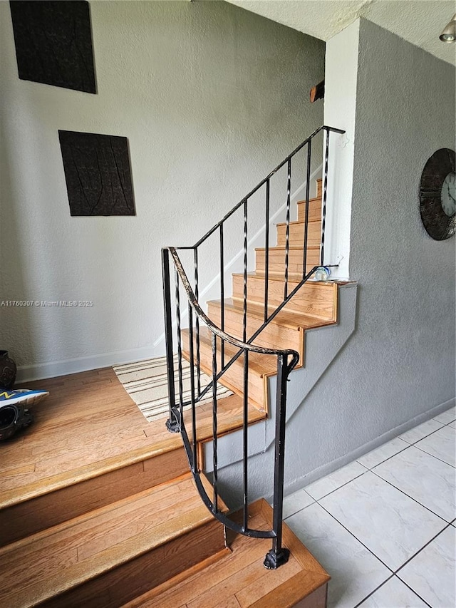 staircase with wood finished floors, a textured wall, and baseboards