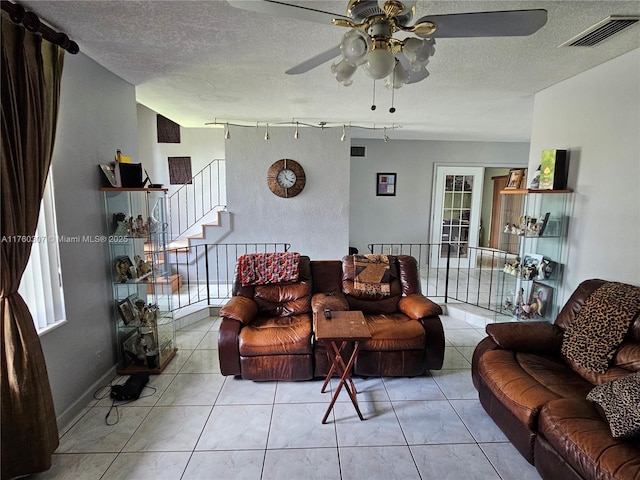 living room featuring stairway, light tile patterned floors, visible vents, and a textured ceiling