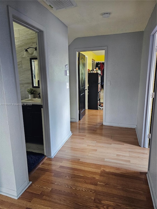 corridor featuring visible vents, baseboards, wood finished floors, and a textured wall