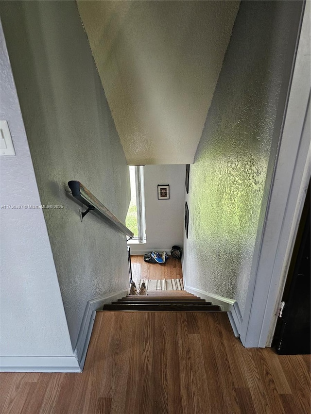 stairs with wood finished floors, a textured wall, and baseboards