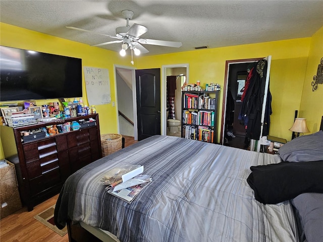 bedroom with ceiling fan, visible vents, a textured ceiling, and wood finished floors