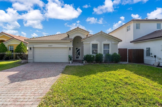 mediterranean / spanish home with stucco siding, a front lawn, decorative driveway, fence, and a garage