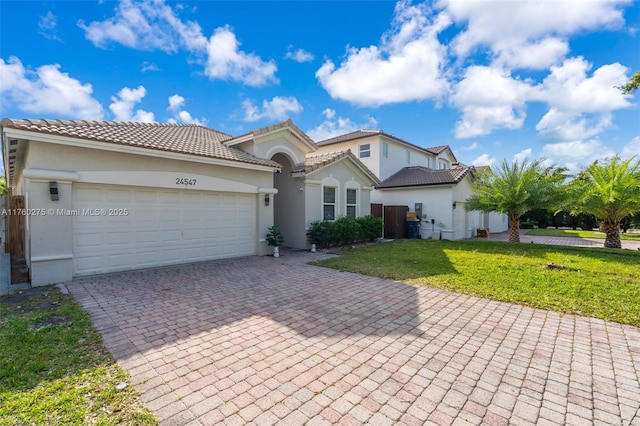 mediterranean / spanish house with a tiled roof, a front yard, stucco siding, decorative driveway, and an attached garage