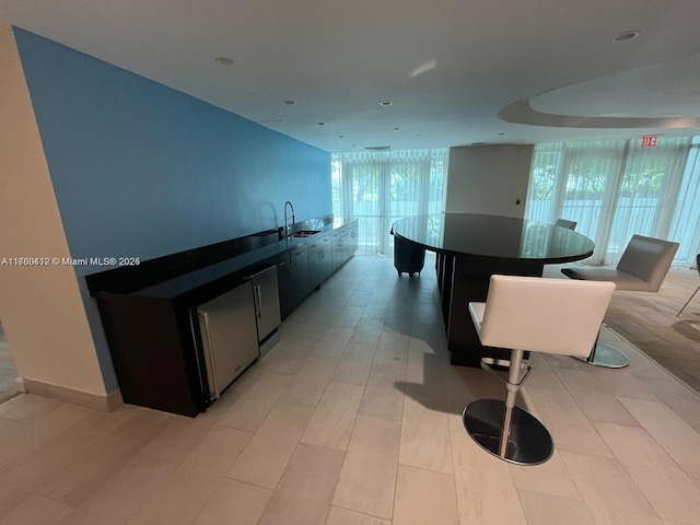 kitchen featuring an island with sink, recessed lighting, dark cabinetry, light wood-style floors, and a sink