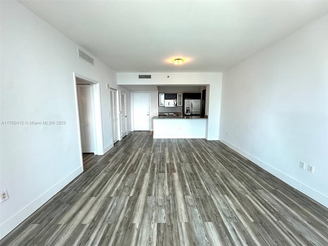 unfurnished living room featuring dark wood-type flooring, baseboards, and visible vents