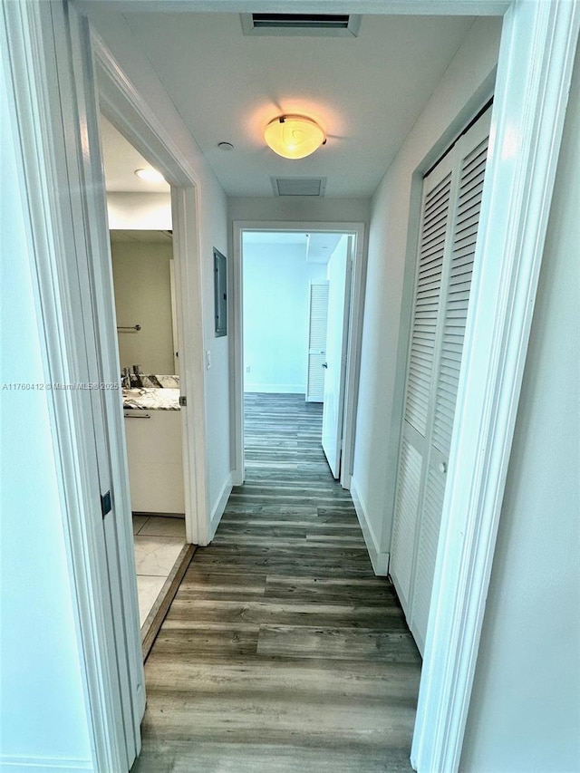 hallway with dark wood finished floors, electric panel, baseboards, and visible vents