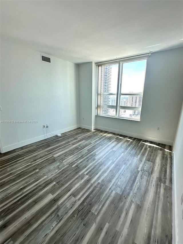 empty room with visible vents, baseboards, and dark wood-style floors