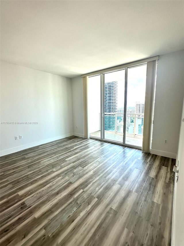 unfurnished room with a wall of windows, wood finished floors, and baseboards