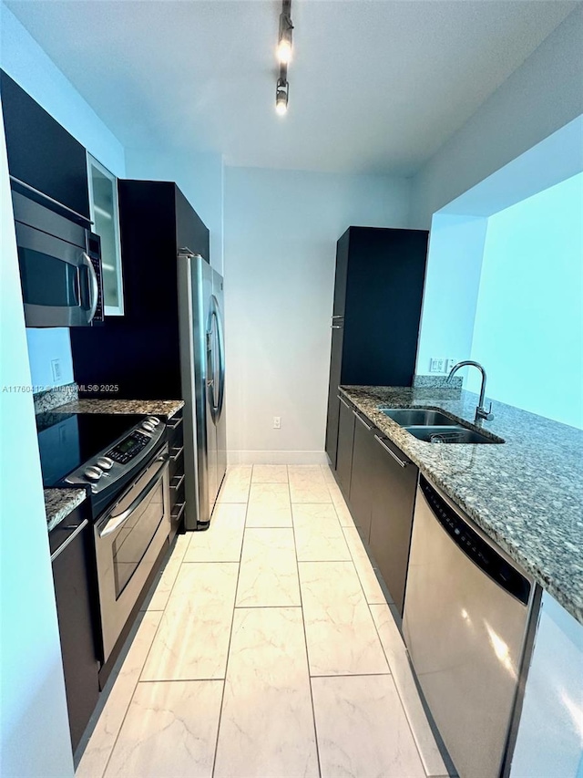 kitchen featuring dark cabinetry, dark stone countertops, a sink, appliances with stainless steel finishes, and marble finish floor