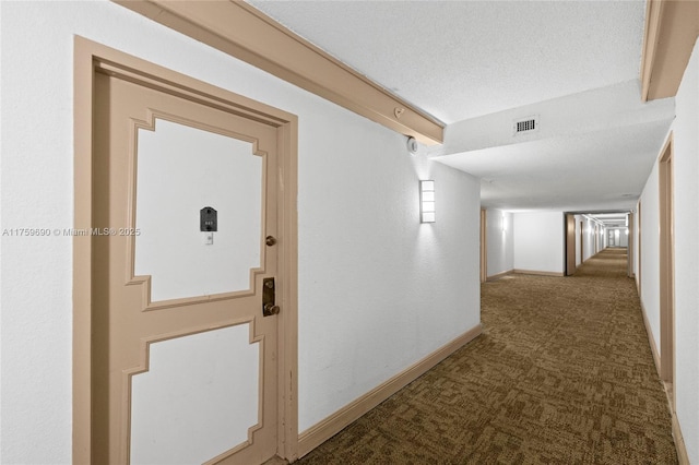 hall with visible vents, a textured ceiling, baseboards, and carpet