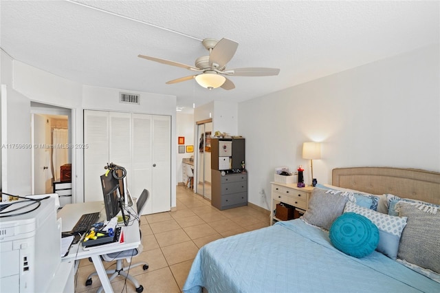 bedroom with a ceiling fan, visible vents, light tile patterned flooring, a closet, and a textured ceiling