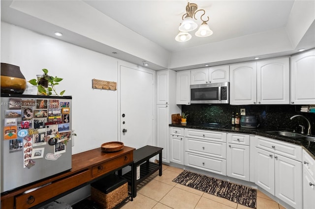 kitchen with stainless steel microwave, backsplash, light tile patterned floors, white cabinetry, and a sink