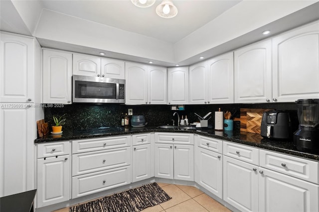 kitchen featuring a sink, stainless steel microwave, white cabinetry, light tile patterned floors, and decorative backsplash