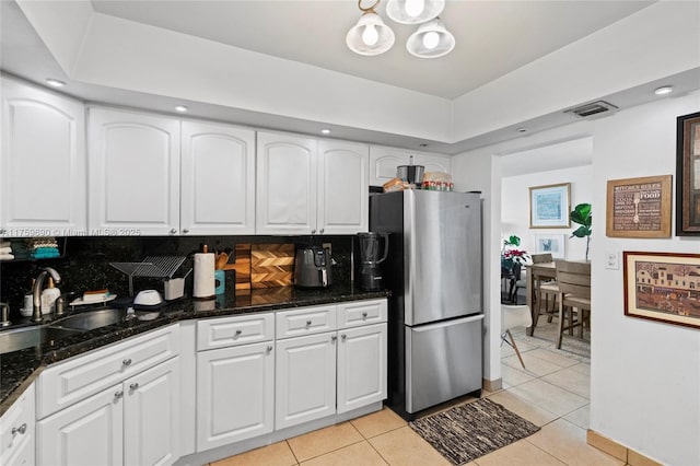 kitchen with a sink, tasteful backsplash, freestanding refrigerator, light tile patterned flooring, and white cabinets