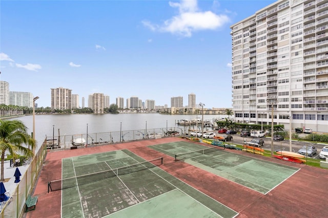 view of tennis court with a city view, fence, and a water view