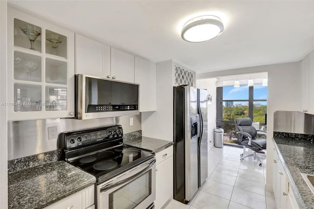 kitchen with glass insert cabinets, dark stone countertops, light tile patterned flooring, white cabinets, and stainless steel appliances