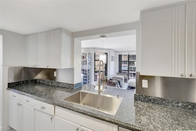 kitchen featuring dark stone counters, white cabinets, and a sink