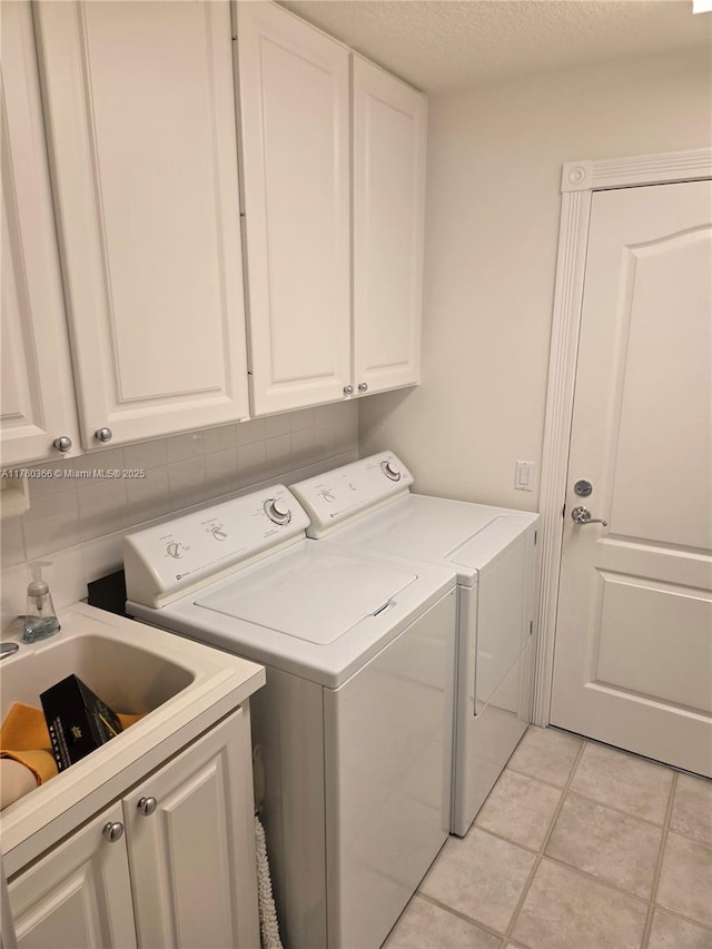 clothes washing area featuring a textured ceiling, light tile patterned floors, cabinet space, and washer and clothes dryer