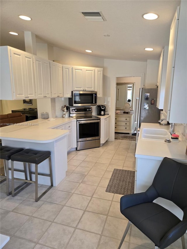 kitchen featuring visible vents, a peninsula, a sink, stainless steel appliances, and light countertops