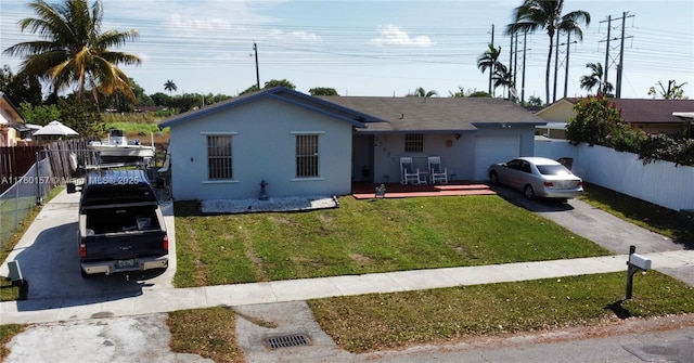 view of front facade with a front yard, fence, an attached garage, stucco siding, and aphalt driveway